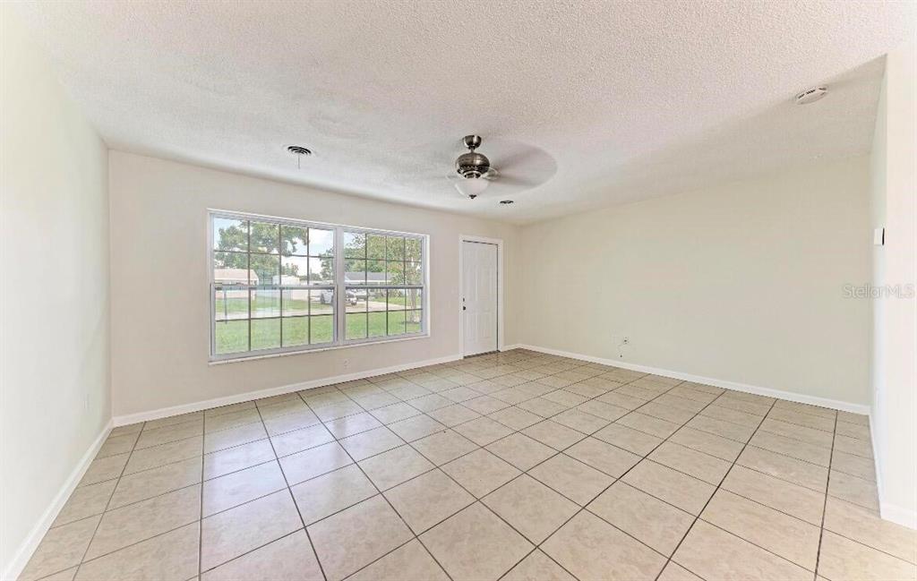 An empty room with beige tile flooring, a ceiling fan, and a large window — 3207 19TH AVENUE W, BRADENTON, FL
