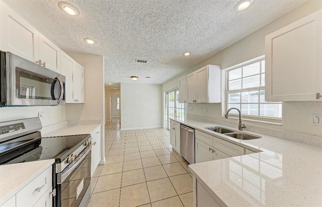 A kitchen with white cabinets, light countertops, stainless steel appliances, and tiled flooring — 3207 19TH AVENUE W, BRADENTON, FL