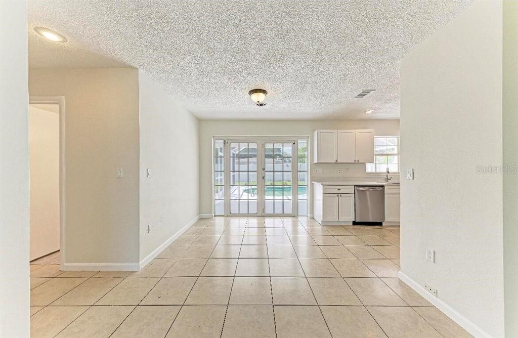 A tiled dining area leads to a kitchen with white cabinets and a backyard view — 3207 19TH AVENUE W, BRADENTON, FL