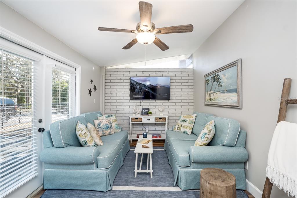 A living room features two light blue sofas, a brick accent wall, and a ceiling fan — 2213 WASON ROAD UNIT 1, SARASOTA, FL