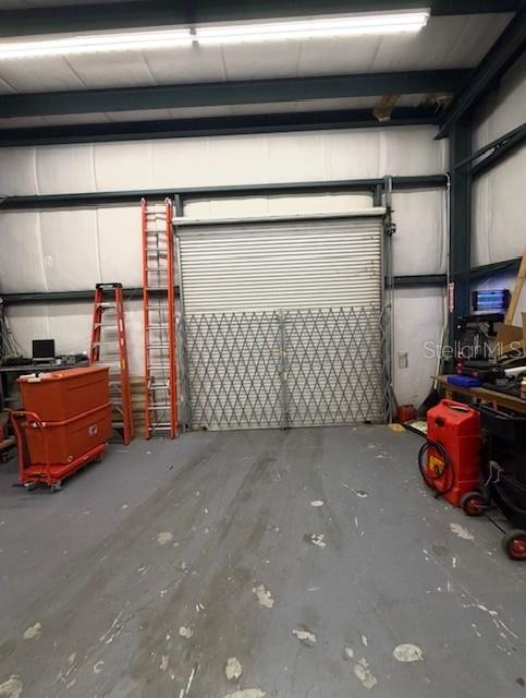 An industrial warehouse space features a large roll-up door, a metal security gate, and storage equipment — 483 NW 68TH AVENUE, OCALA, FL