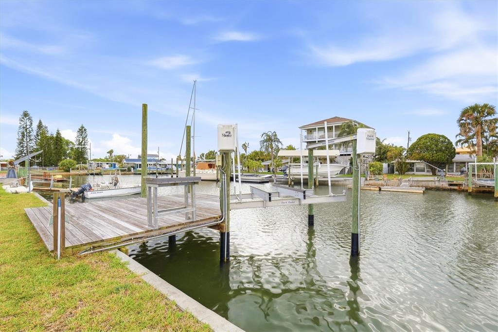 A wooden boat dock with a mechanical lift sits along a canal near houses — 13603 BRITTON DRIVE, HUDSON, FL