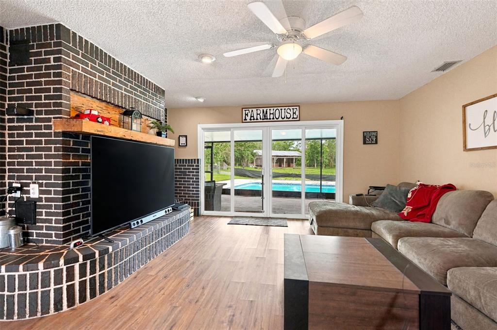 A living room features a dark brick fireplace, a large television, and sliding glass doors — 9550 PURDY STREET, SPRING HILL, FL