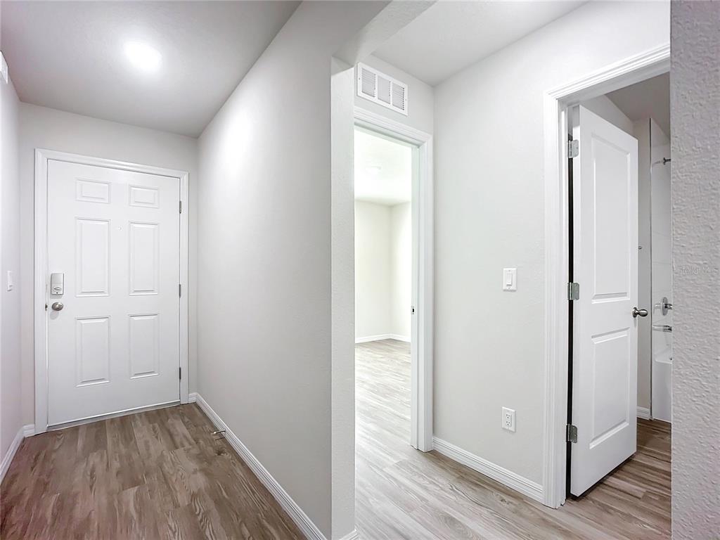 A hallway with light wood-look flooring leads to an open doorway and a closed door — 38 SLUMBER MEADOW TRAIL, PALM COAST, FL