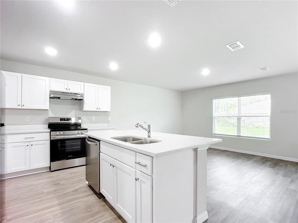 A modern kitchen features white cabinets, a central island with a sink, and stainless appliances — 38 SLUMBER MEADOW TRAIL, PALM COAST, FL