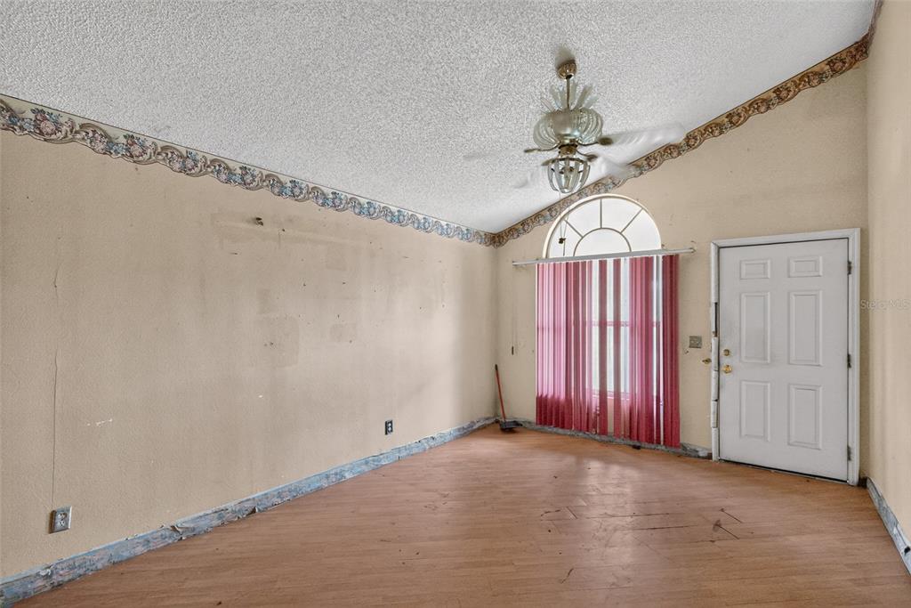 An empty room with wood-look flooring, a ceiling fan, wallpaper border, and a white door — 1301 W 11TH STREET, SANFORD, FL