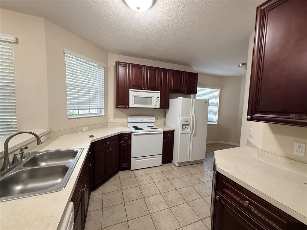 A kitchen features dark wood cabinets, white appliances, laminate countertops, and light-colored tile flooring — 10547 REGENT SQUARE DRIVE UNIT 1008, ORLANDO, FL