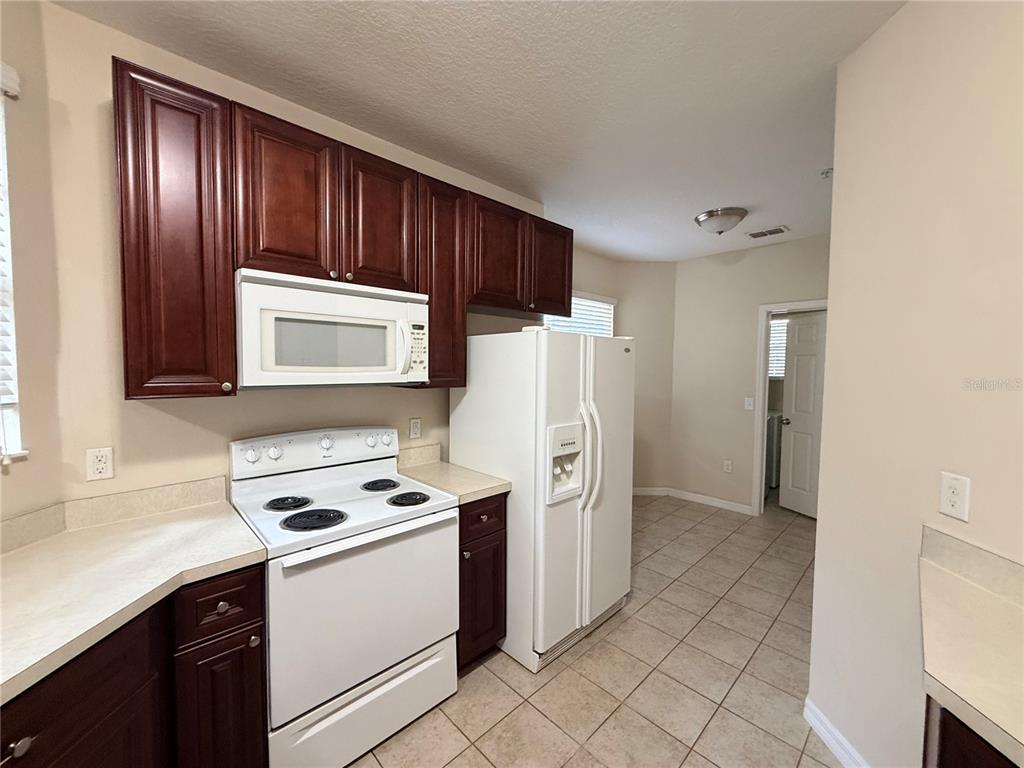 A kitchen features dark wood cabinets, white appliances, beige countertops, and light tile flooring — 10547 REGENT SQUARE DRIVE UNIT 1008, ORLANDO, FL