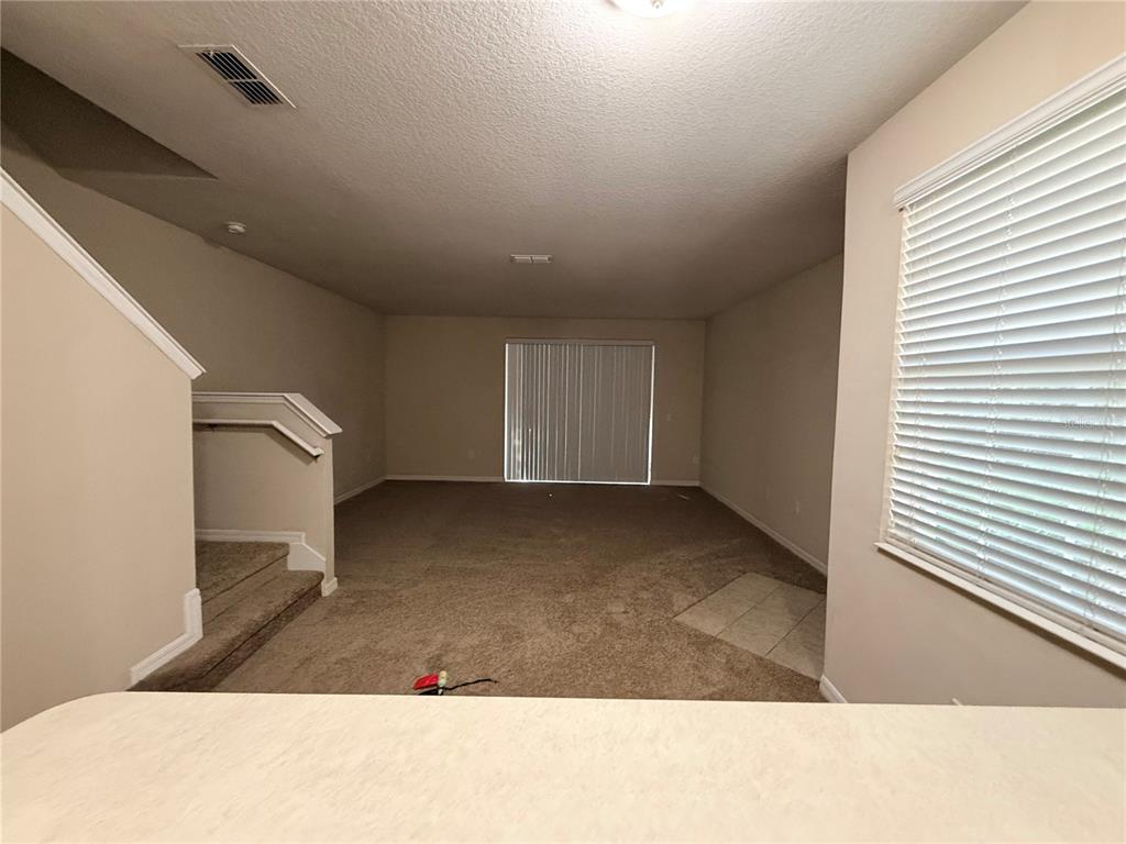 An empty living room features beige carpeting, a staircase, and sliding glass doors — 10547 REGENT SQUARE DRIVE UNIT 1008, ORLANDO, FL