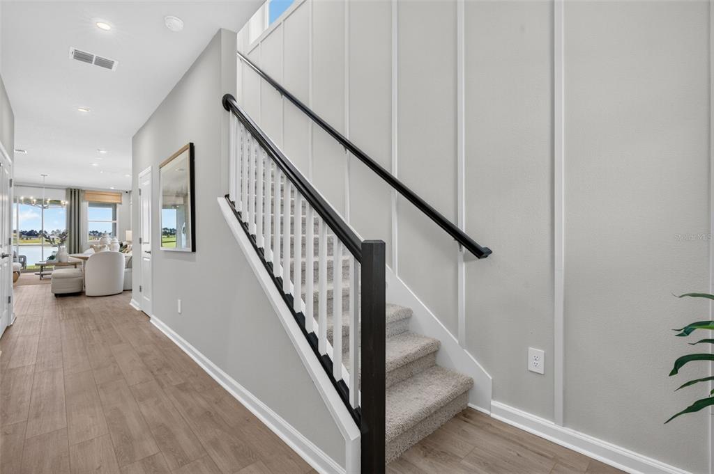 A hallway features wood-look flooring, a carpeted staircase with a black railing, and board-and-batten walls — 34854 ARBOR RETREAT DRIVE, DADE CITY, FL