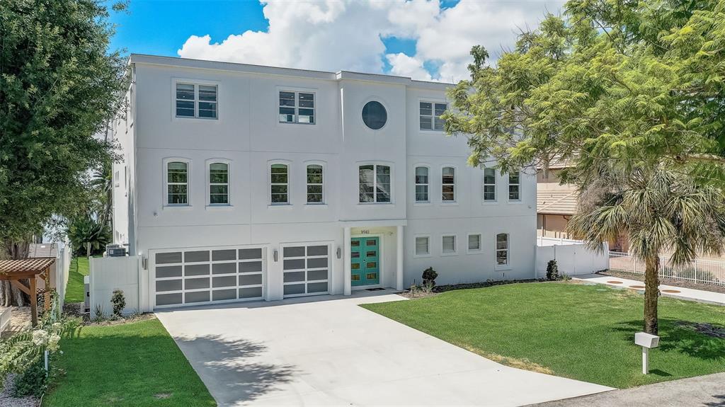 A three-story white house features a teal front door, two garage doors, and a driveway — 9940 LONE TREE LANE, ORLANDO, FL