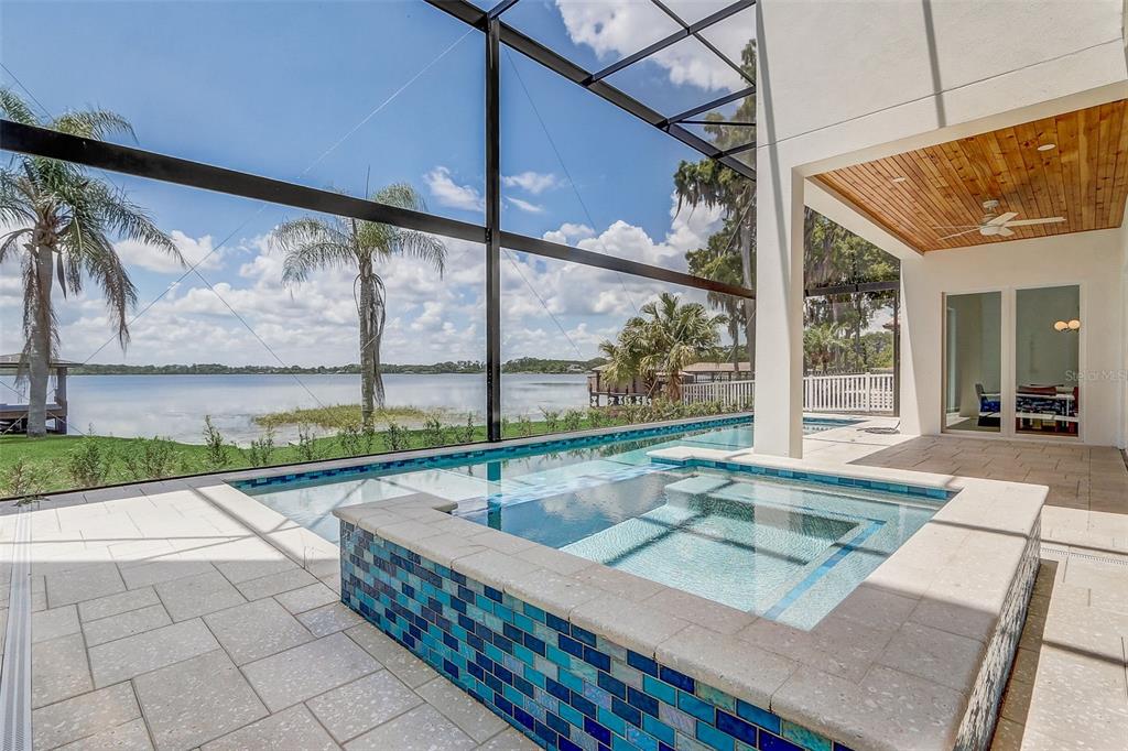 A screened-in patio features a tiled hot tub and pool overlooking a lake — 9940 LONE TREE LANE, ORLANDO, FL