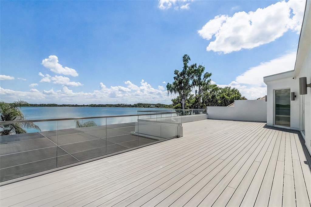 A spacious outdoor deck with light-colored composite flooring and a glass railing overlooking a lake — 9940 LONE TREE LANE, ORLANDO, FL