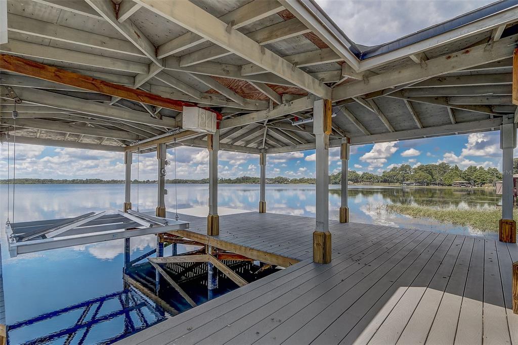 A covered wooden boat dock with a boat lift overlooking a calm lake — 9940 LONE TREE LANE, ORLANDO, FL
