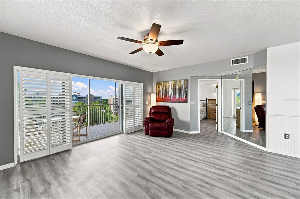 A living room features gray wood-look flooring, a red recliner, and a balcony with shutters — 960 STARKEY ROAD UNIT 3501, LARGO, FL