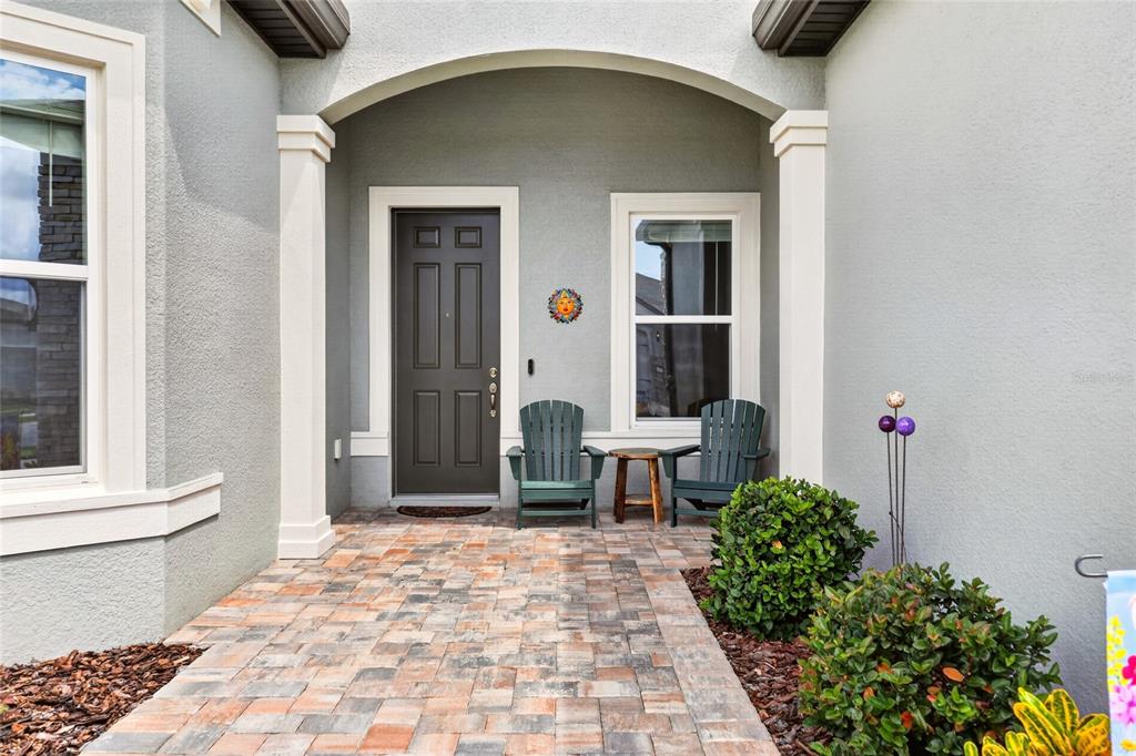 A paved entryway features a dark front door, two chairs, and a small side table — 5235 SW 88TH CIRCLE, OCALA, FL