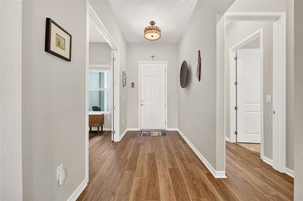 A hallway with wood-look flooring leads to a white front door under a ceiling light — 5235 SW 88TH CIRCLE, OCALA, FL
