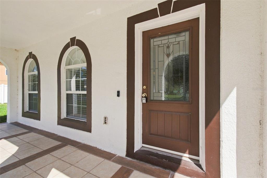 A covered porch features a brown front door and two arched windows on a white wall — 5155 SPANISH OAKS DRIVE, LAKELAND, FL