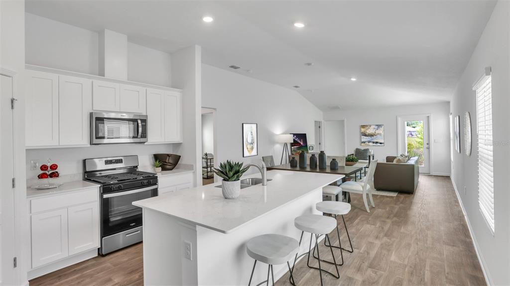 A modern open-concept kitchen features white cabinetry, a quartz island with barstools, and wood flooring — 838 GRAND RESERVE DRIVE, BUNNELL, FL