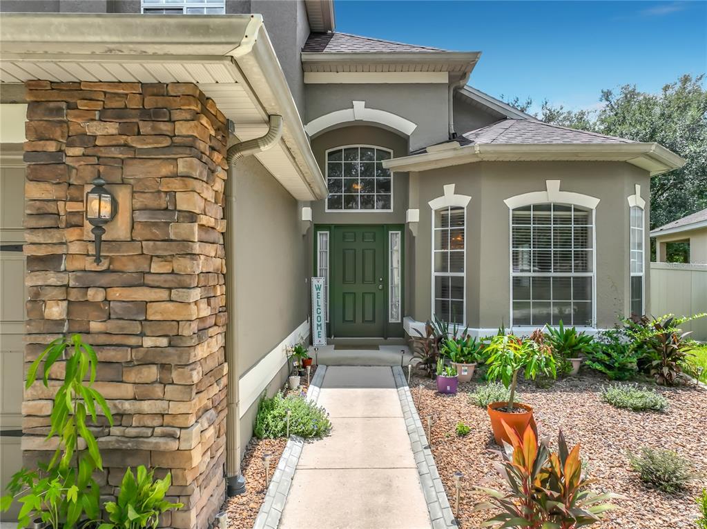 A stone-accented exterior features a green front door, a concrete walkway, and landscaped garden beds — 9038 VICKROY TERRACE, OVIEDO, FL