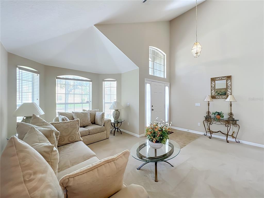 A living room with vaulted ceilings, beige carpet, a glass coffee table, and a front entrance — 9038 VICKROY TERRACE, OVIEDO, FL