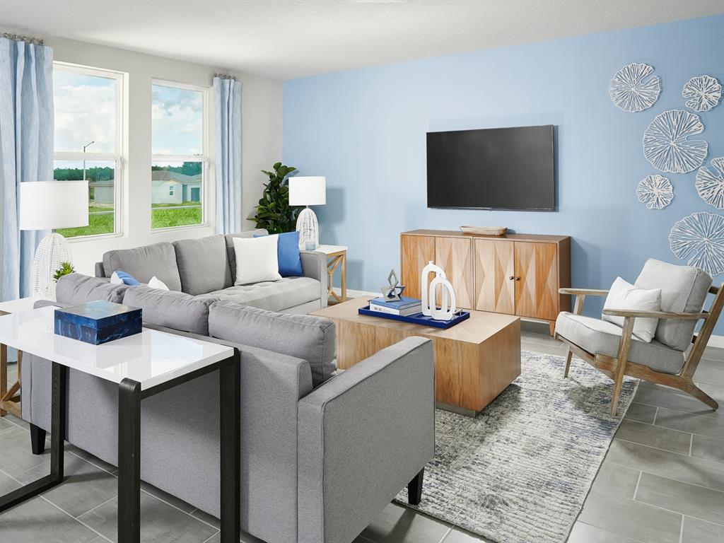A living room features a grey sofa, wooden coffee table, television, and light blue walls — 2888 WILD OLIVE DRIVE, ST CLOUD, FL