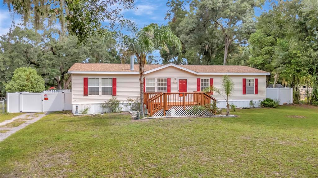 A single-story manufactured home with light siding, red shutters, and a wooden front deck — 2716 SEMINOLE TRAIL, LEESBURG, FL