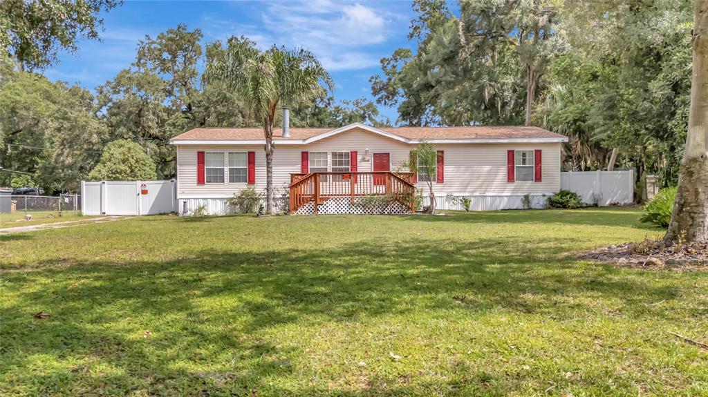 A single-story manufactured home with light siding, red shutters, and a wooden front deck — 2716 SEMINOLE TRAIL, LEESBURG, FL