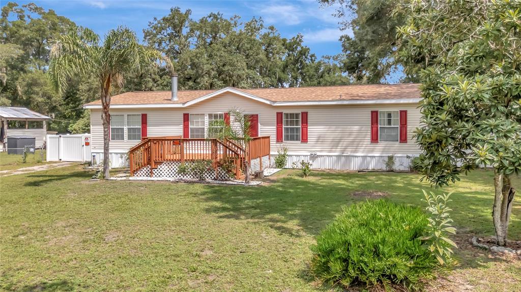 A single-story manufactured home with light siding, red shutters, and a wooden front deck — 2716 SEMINOLE TRAIL, LEESBURG, FL