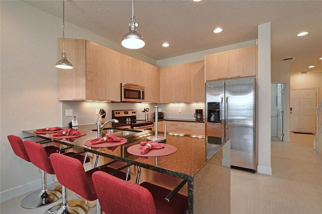 A kitchen features light wood cabinets, a dark granite island, and red bar stools — 1523 STILL DRIVE, CLERMONT, FL