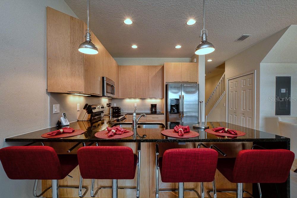 A kitchen features light wood cabinets, black granite countertops, and four red bar stools — 1523 STILL DRIVE, CLERMONT, FL