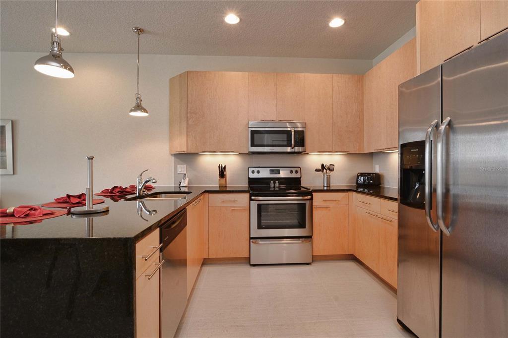 A modern kitchen features light wood cabinets, stainless steel appliances, and black granite countertops — 1523 STILL DRIVE, CLERMONT, FL