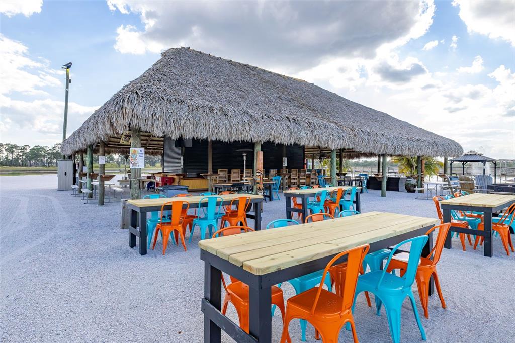 An outdoor tiki bar features a thatched roof, gravel ground, and colorful metal patio furniture — 96 CR-630 E, LAKE WALES, FL