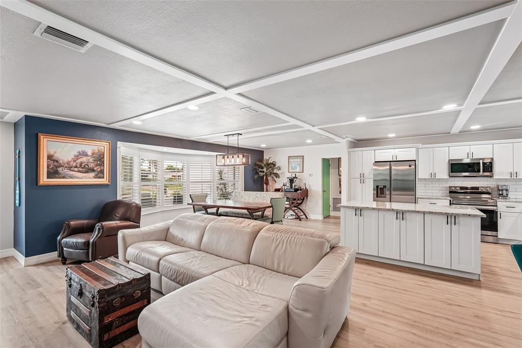 An open-concept living room and kitchen featuring white cabinetry, a sectional sofa, and coffered ceilings — 365 SHAMROCK BOULEVARD, VENICE, FL