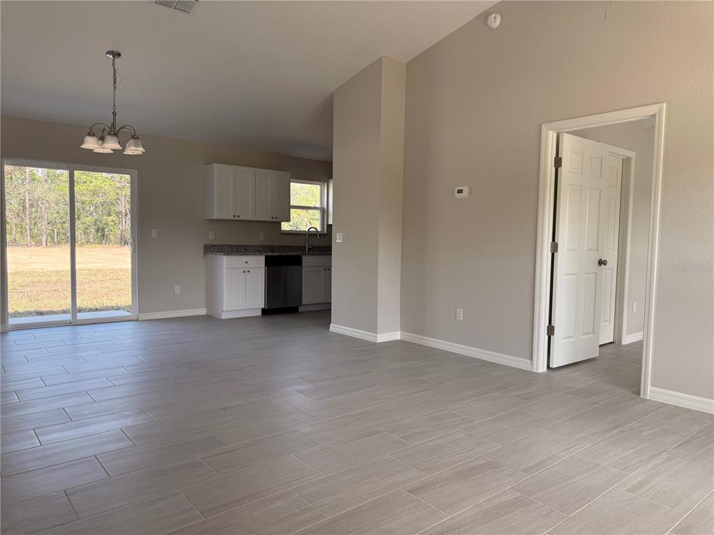 An open-concept living area features light gray tile flooring, a kitchen with white cabinets, and a sliding glass door — 4730 SW KERRIA COURT, DUNNELLON, FL