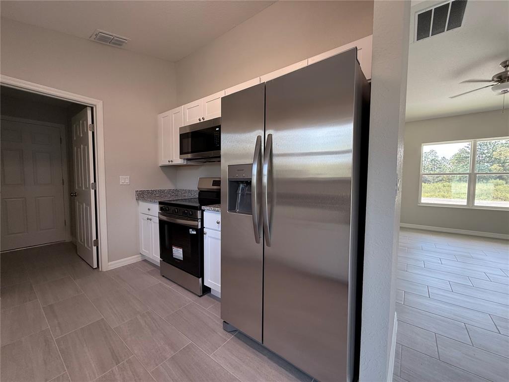A kitchen features stainless steel appliances, white cabinets, granite countertops, and light-colored tile flooring — 4730 SW KERRIA COURT, DUNNELLON, FL