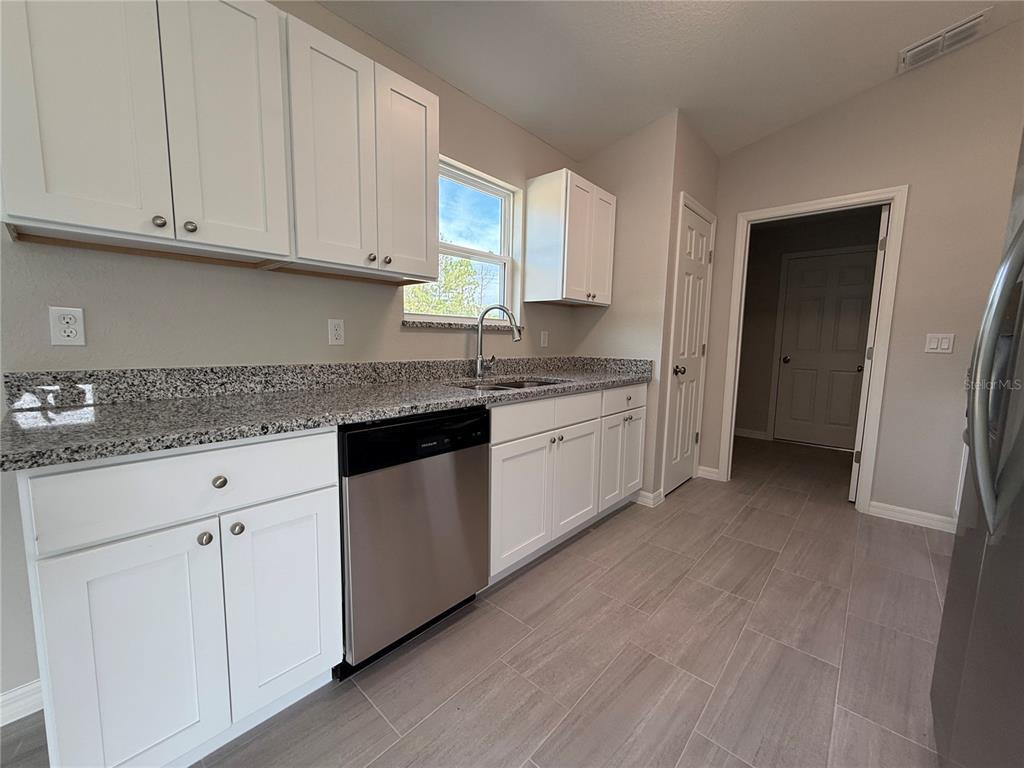 A kitchen features white cabinets, granite countertops, stainless steel appliances, and light-colored tile flooring — 4730 SW KERRIA COURT, DUNNELLON, FL