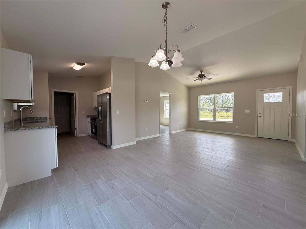 An open-concept living area features light gray tile flooring, a kitchen, and a chandelier — 4730 SW KERRIA COURT, DUNNELLON, FL