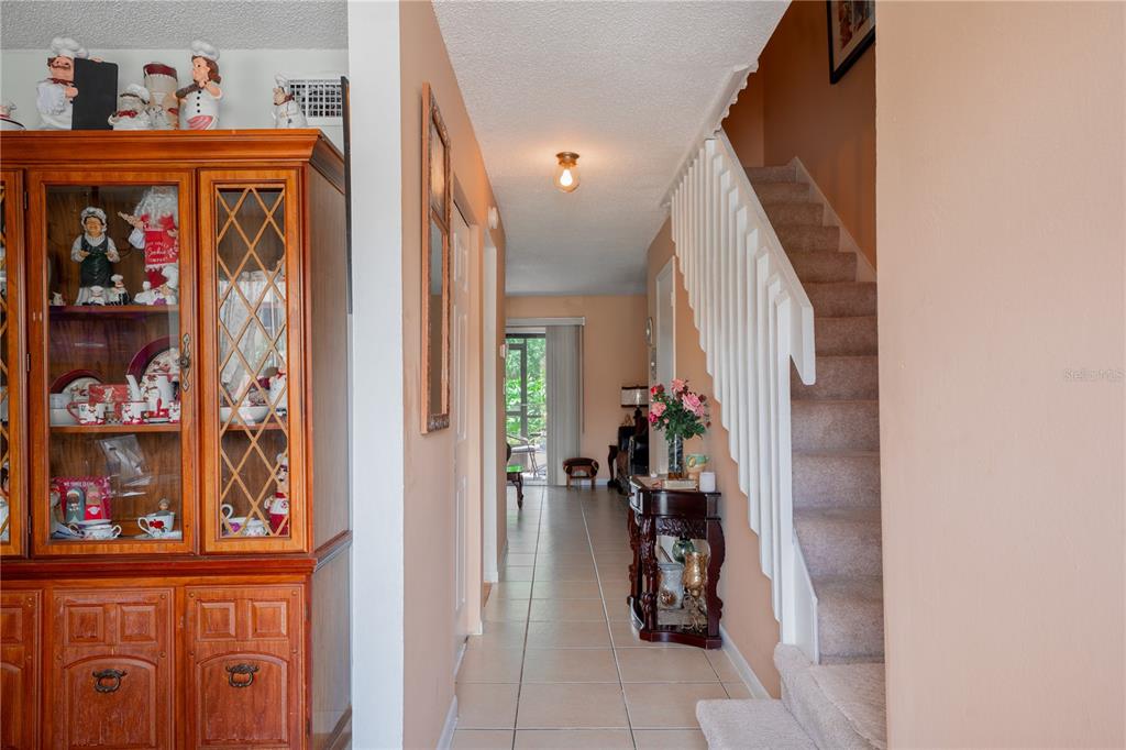 A hallway with tile flooring leads to a living area past a staircase and hutch — 5038 DOWNING STREET UNIT 7, ORLANDO, FL