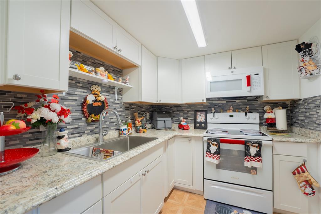 A kitchen features white cabinets, granite countertops, a tiled backsplash, and white appliances — 5038 DOWNING STREET UNIT 7, ORLANDO, FL