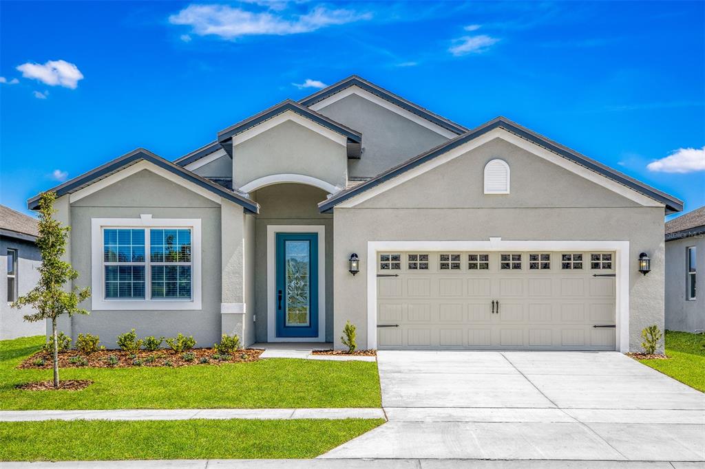 A single-story house with a gray stucco exterior, a blue front door, and a garage — 3343 CHINOTTO DRIVE, LAKE ALFRED, FL