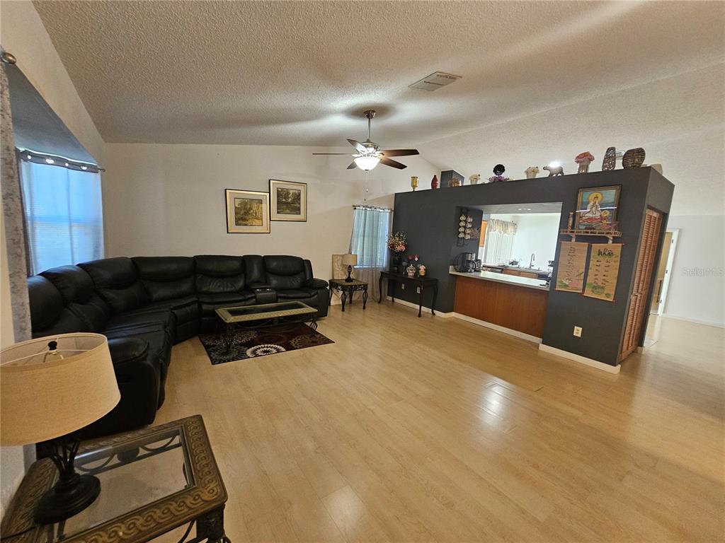 A living room with light wood flooring, a black sectional sofa, and a kitchen pass-through — 1885 FEATHER TREE CIRCLE, CLEARWATER, FL