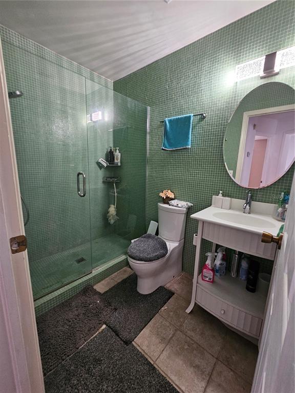 A bathroom features green mosaic tile walls, a glass-enclosed shower, a toilet, and a vanity — 1885 FEATHER TREE CIRCLE, CLEARWATER, FL