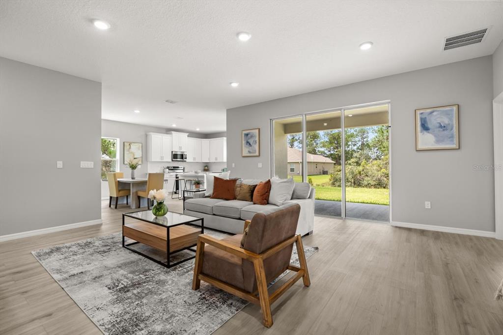A living room with light wood floors, a gray sofa, and a view of the backyard — 6754 COCONUT GROVE DRIVE, SEBRING, FL
