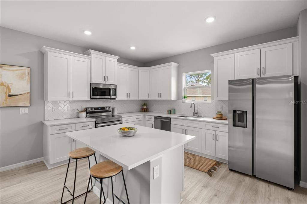 A modern kitchen features white cabinetry, stainless steel appliances, a center island, and light flooring — 6754 COCONUT GROVE DRIVE, SEBRING, FL