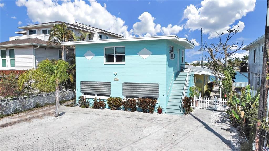 A light blue two-story house features an exterior staircase and a paved driveway — 11215 3RD STREET E, TREASURE ISLAND, FL