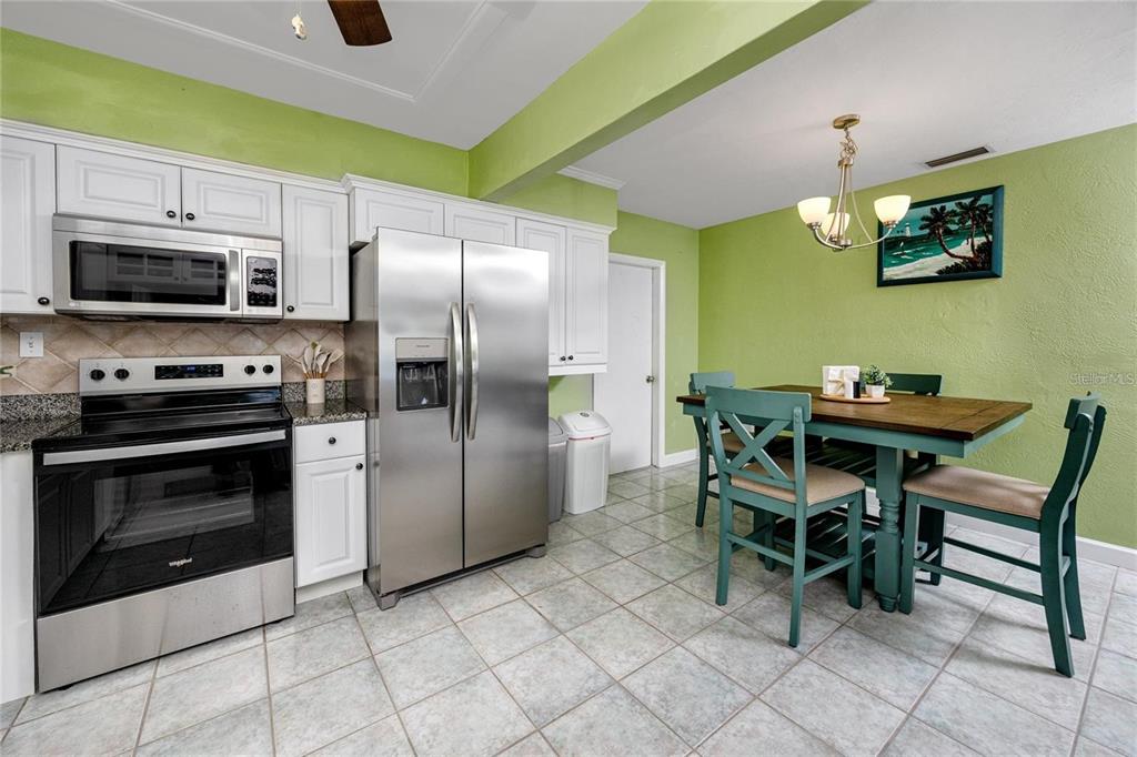 A kitchen with white cabinets, stainless steel appliances, green walls, and a dining table set — 11215 3RD STREET E, TREASURE ISLAND, FL
