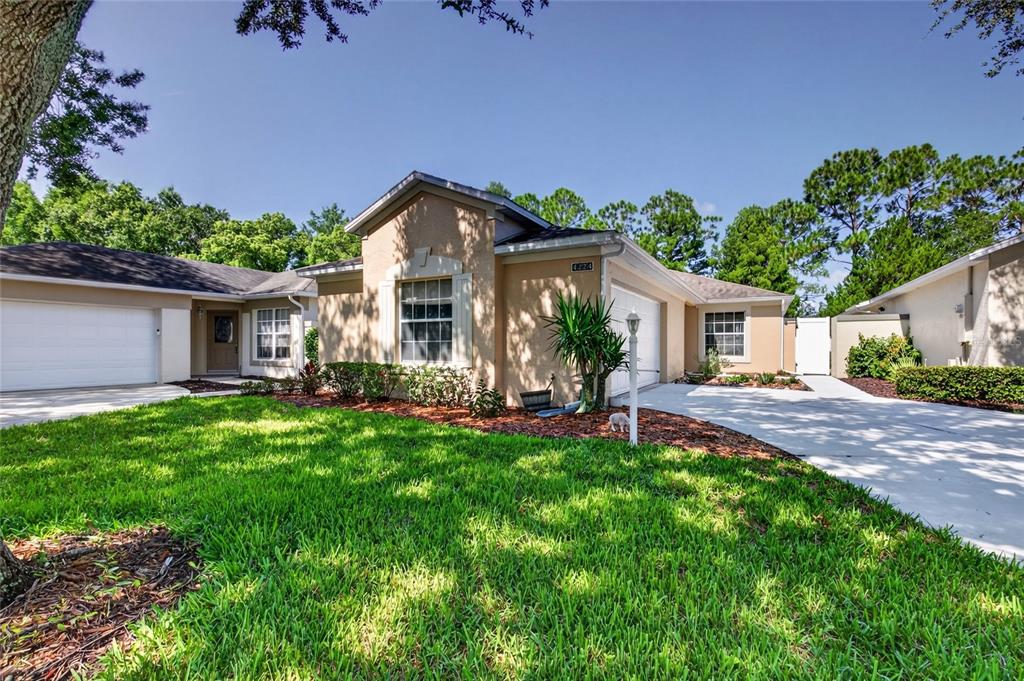 A tan single-story house with a two-car garage and a green lawn under a blue sky — 4224 SNOWDON STREET, CLERMONT, FL