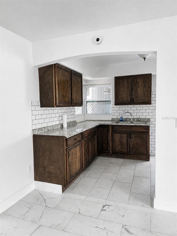 A kitchen features dark wood cabinets, granite countertops, white subway tile backsplash, and marble-look flooring — 1315 E HANCOCK DRIVE, DELTONA, FL