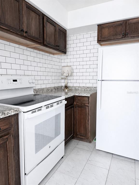 A kitchen features dark wood cabinets, white subway tile backsplash, granite countertops, and white appliances — 1315 E HANCOCK DRIVE, DELTONA, FL